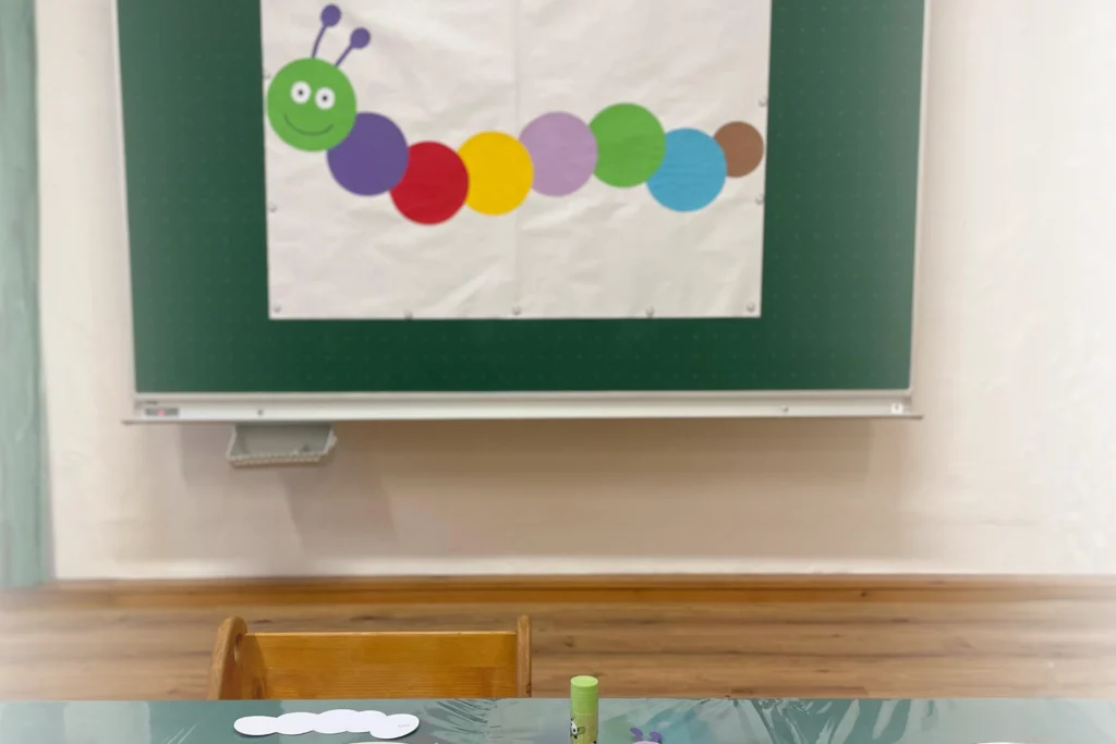 Eine bunte Raupe aus Papier an einer grünen Schultafel in einem Gruppenraum für Kinder im Familienzentrum Schärding/Andorf.