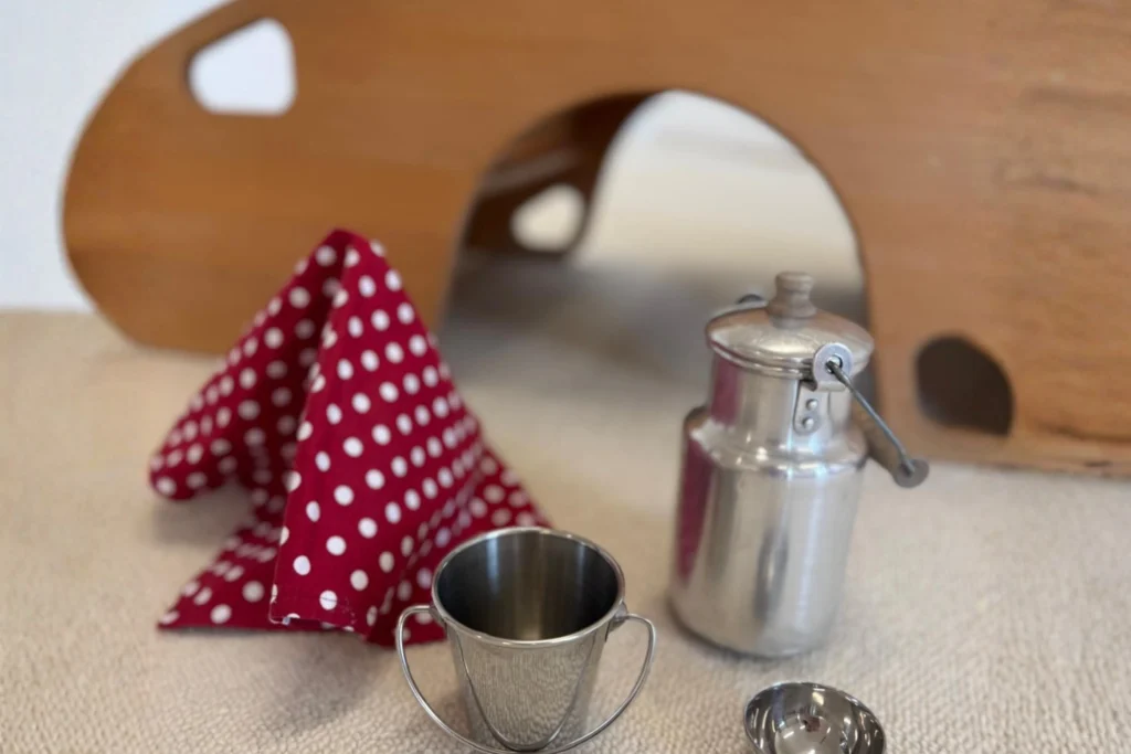 Spielzeug-Küchenutensilien aus Metall mit einem rot-weiß gepunkteten Tuch vor einem hölzernen Spielbogen im Familienzentrum.