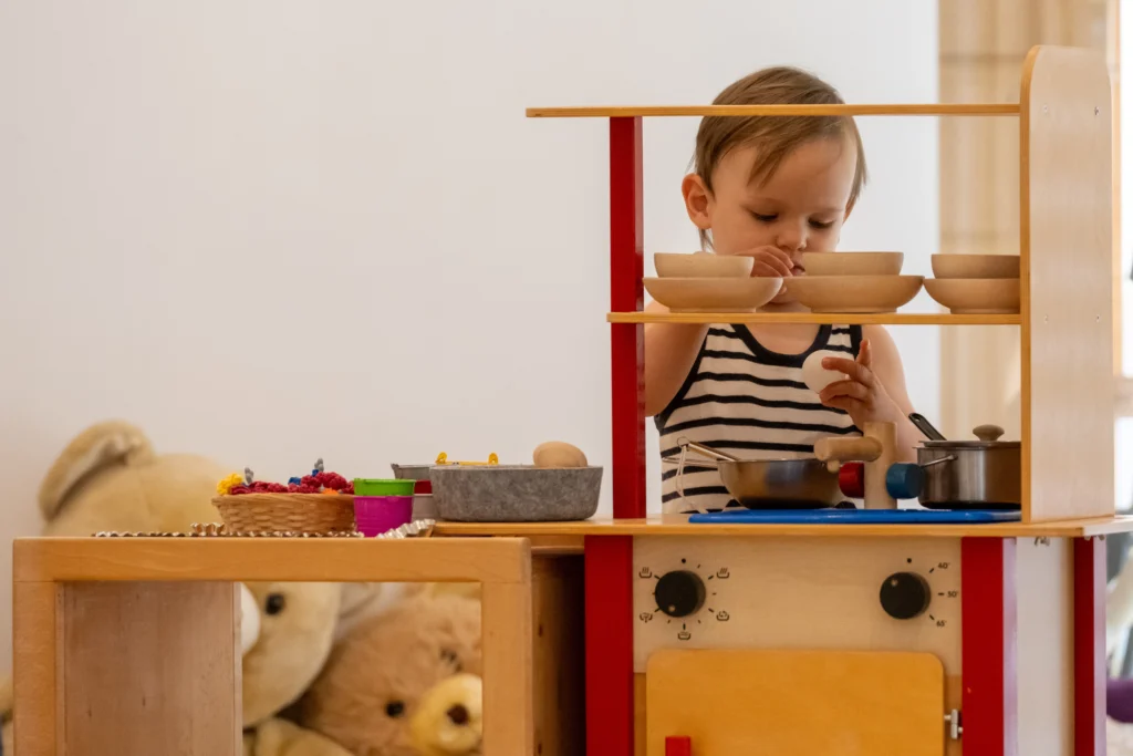 Ein Kleinkind spielt konzentriert in einer Kinderküche aus Holz mit Kochgeschirr und Zubehör im Familienzentrum.
