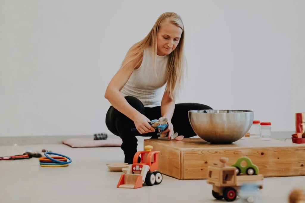 Eine Frau spielt in einem Familienzentrum mit Holzspielzeug und einer Metallschüssel, umgeben von verschiedenen Spielsachen.