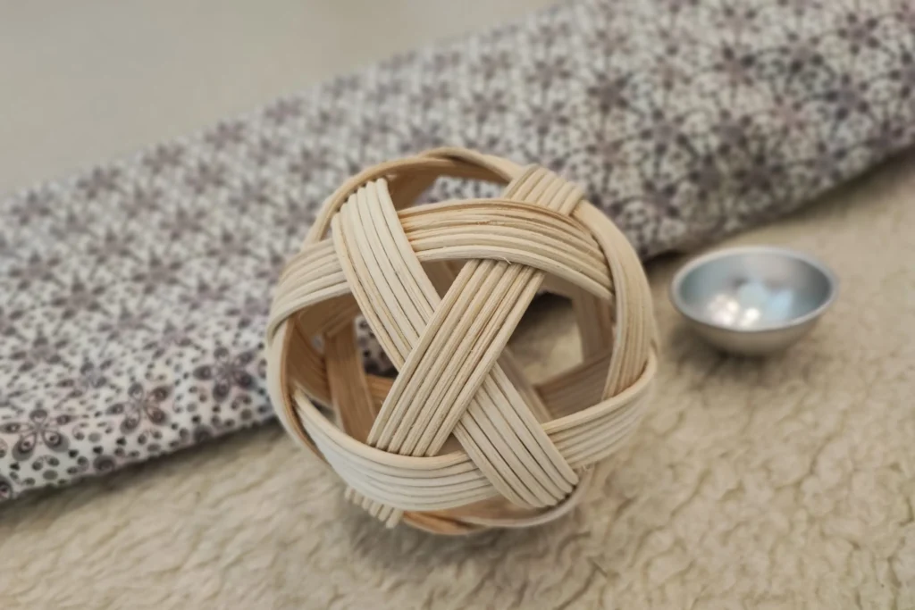 Ein dekorativer, handgeflochtener Ball aus hellem Naturholz auf einem weichen, gemusterten Untergrund im Familienzentrum.