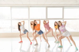 Eine Gruppe junger Frauen in Freizeitkleidung übt gemeinsam eine Tanzchoreografie in einem hellen, modernen Tanzstudio.