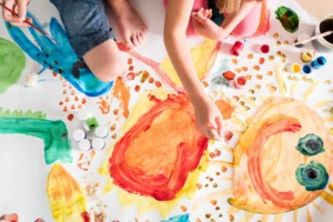 Kinder malen gemeinsam mit bunten Farben auf einem großen Blatt Papier im Familienzentrum Schärding und Andorf.