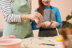 Eine Erwachsene und ein Kind tragen Schürzen und arbeiten gemeinsam an einem Töpferprojekt in einem kreativen Workshop.
