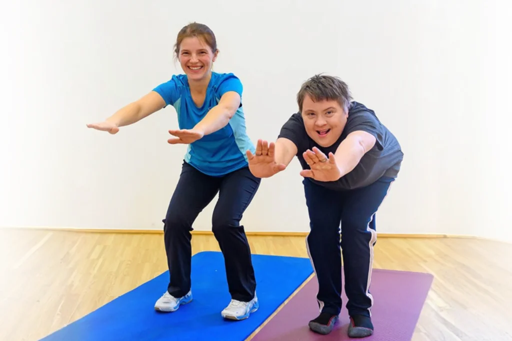Zwei fröhliche Frauen machen gemeinsam Kniebeugen auf Fitnessmatten während eines Sportkurses im Familienzentrum.