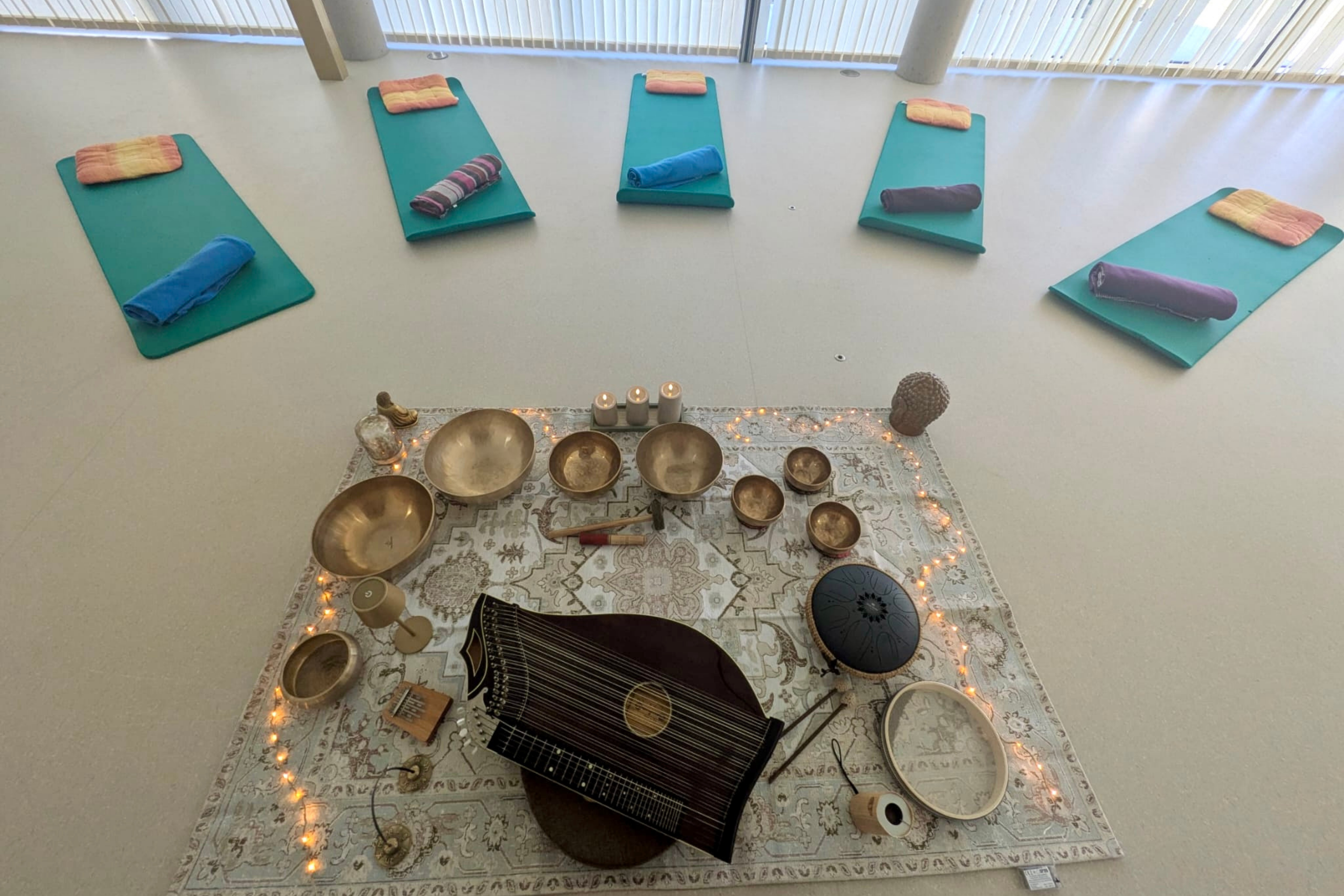 Ein Raum mit Yogamatten und Klangschalen, Zither sowie Kerzen auf einem Teppich für Entspannungsübungen im Familienzentrum.