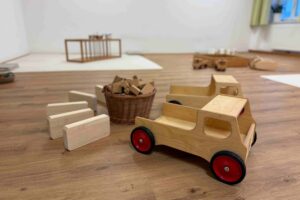 Spielbereich im Familienzentrum mit Holzautos, Bausteinen und einem Weidenkorb auf einem hellen Holzboden für Kinder.