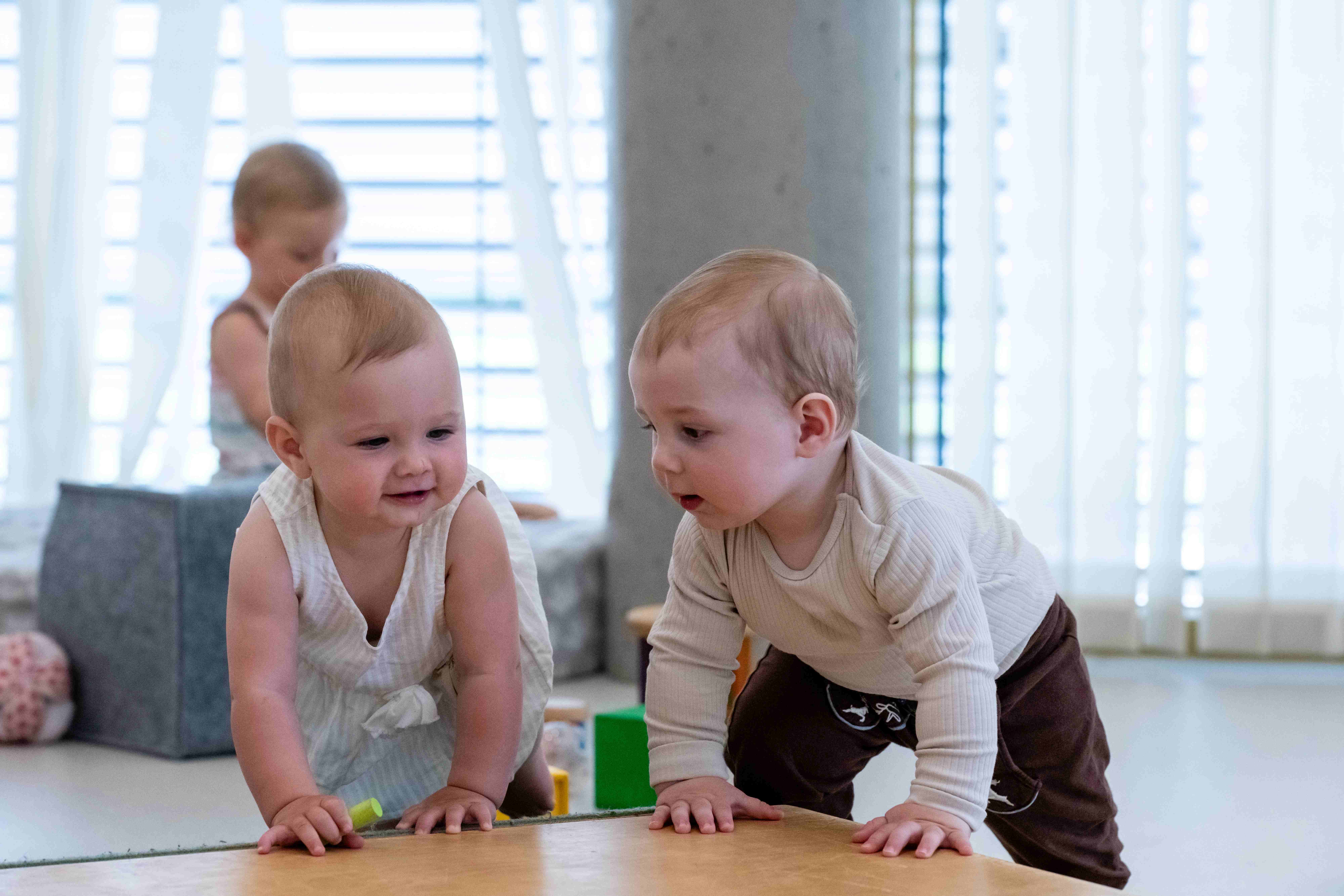 Zwei Kleinkinder krabbeln im Familienzentrum auf einer Matte und spielen gemeinsam in einer hellen, freundlichen Umgebung.