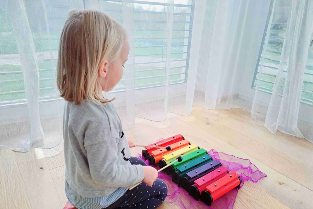 Ein kleines Kind spielt konzentriert auf einem bunten Xylophon während eines Musikangebots im Familienzentrum.