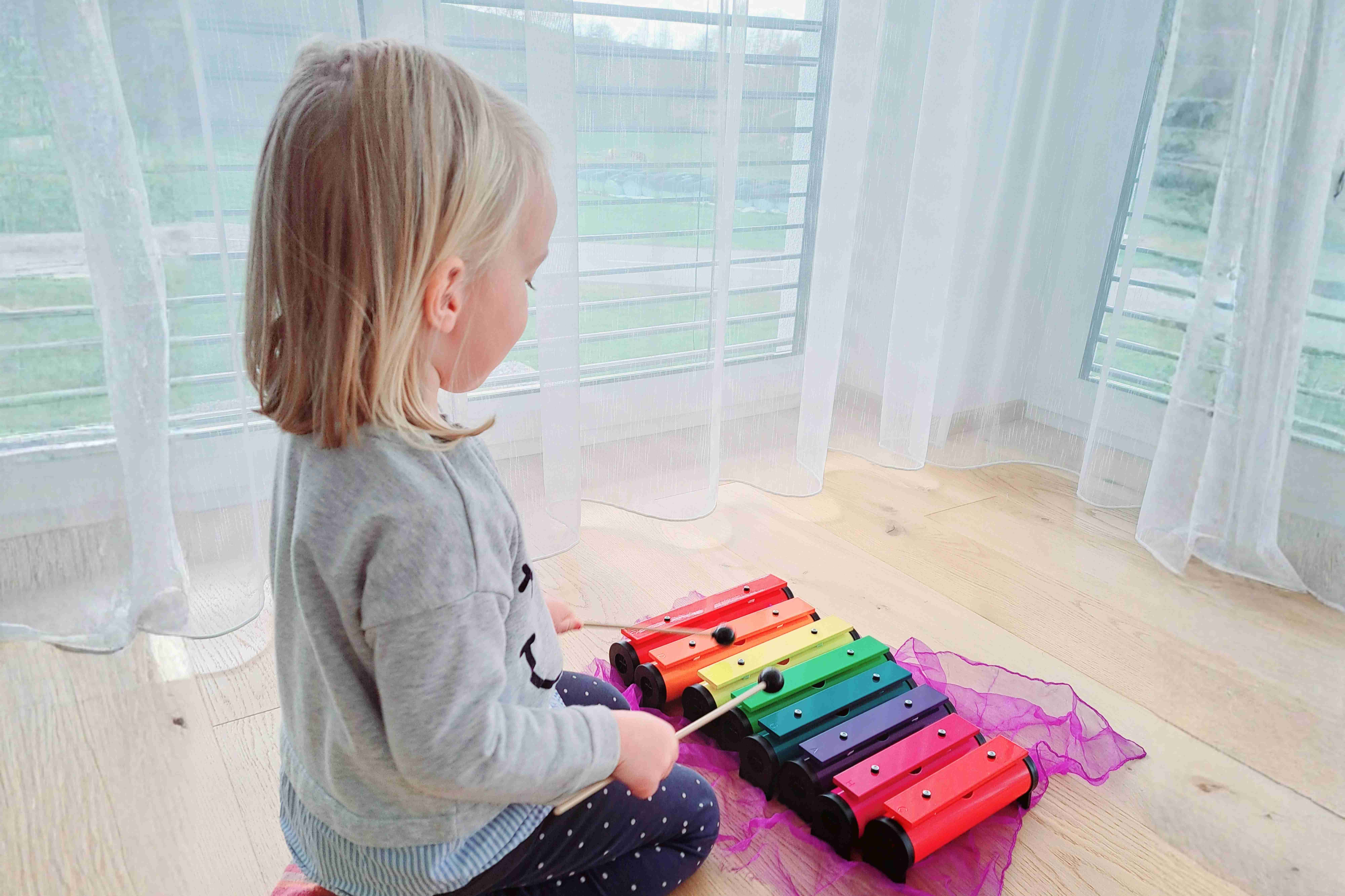 Ein kleines Kind spielt konzentriert auf einem bunten Xylophon während eines Musikangebots im Familienzentrum.