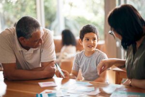 Ein kleiner Junge lernt gemeinsam mit einem Erwachsenen und einer Betreuerin spielerisch mit Lernkarten im Familienzentrum.