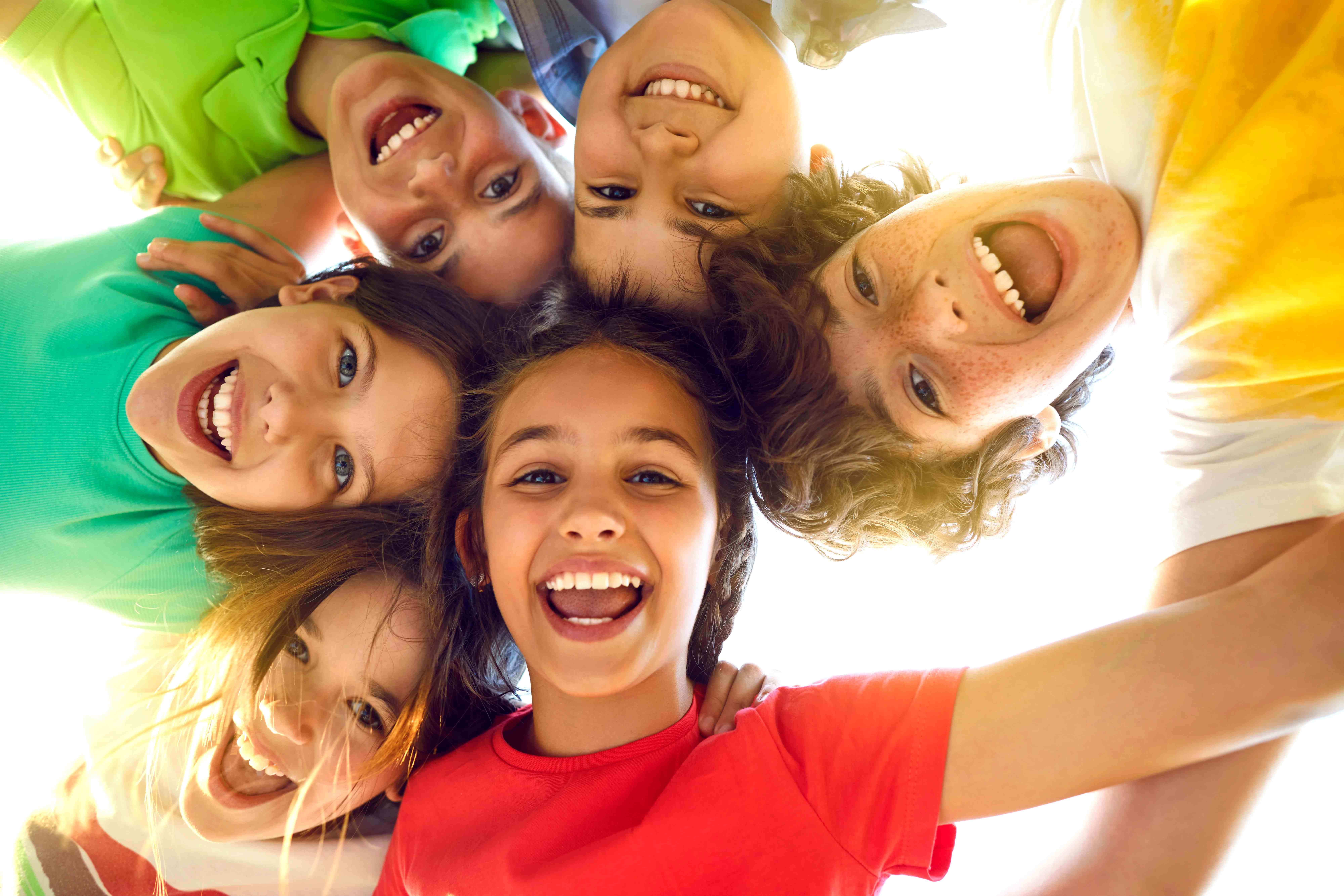 Eine fröhliche Gruppe von Kindern schaut von oben in die Kamera und lacht gemeinsam in einer hellen, freundlichen Umgebung.