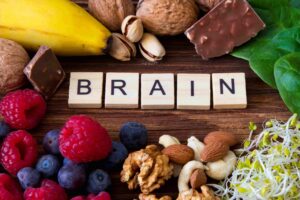 Gesunde Lebensmittel wie Nüsse, Beeren und Bananen umgeben die Buchstabenkacheln mit der Aufschrift BRAIN auf einem Holztisch.