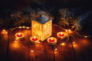 Eine weihnachtliche Laterne mit Sternausschnitten, umgeben von brennenden Teelichtern und einer Lichterkette auf Holz.